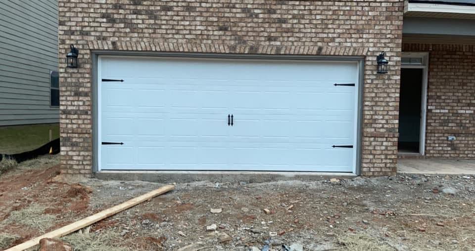 White double garage door set in a brick house exterior with unfinished dirt foreground.