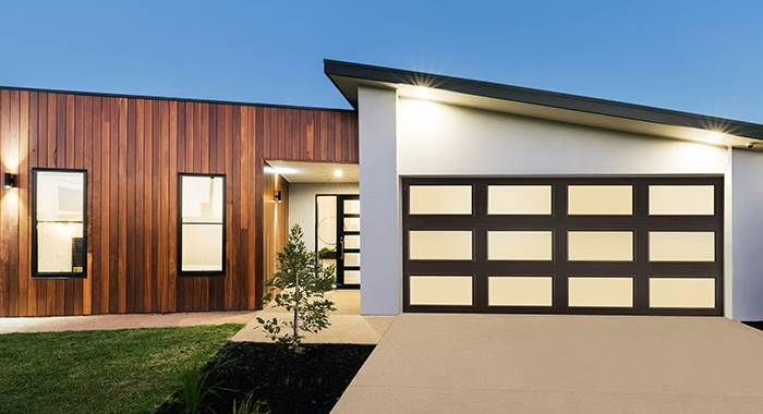 Modern house exterior with wood siding, white garage, and lit windows at dusk