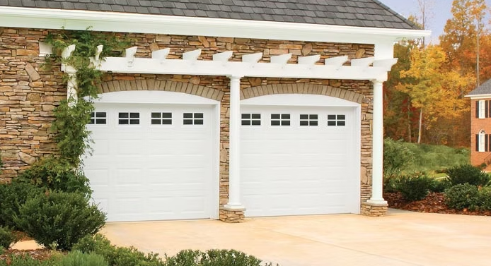 Double white garage doors on a stone house with white trim and a paved driveway