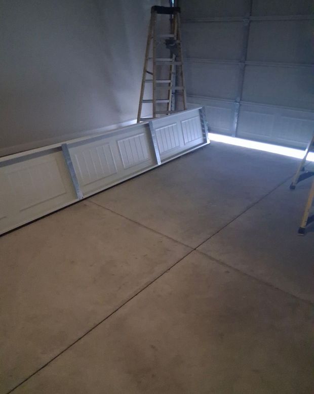 Garage interior with a ladder and several white doors leaning against the wall.