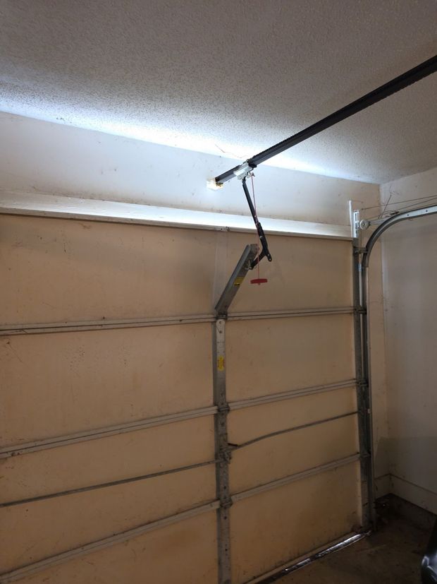 A garage with a sectional door, metal tracks, and a partially open ceiling panel exposing wires.