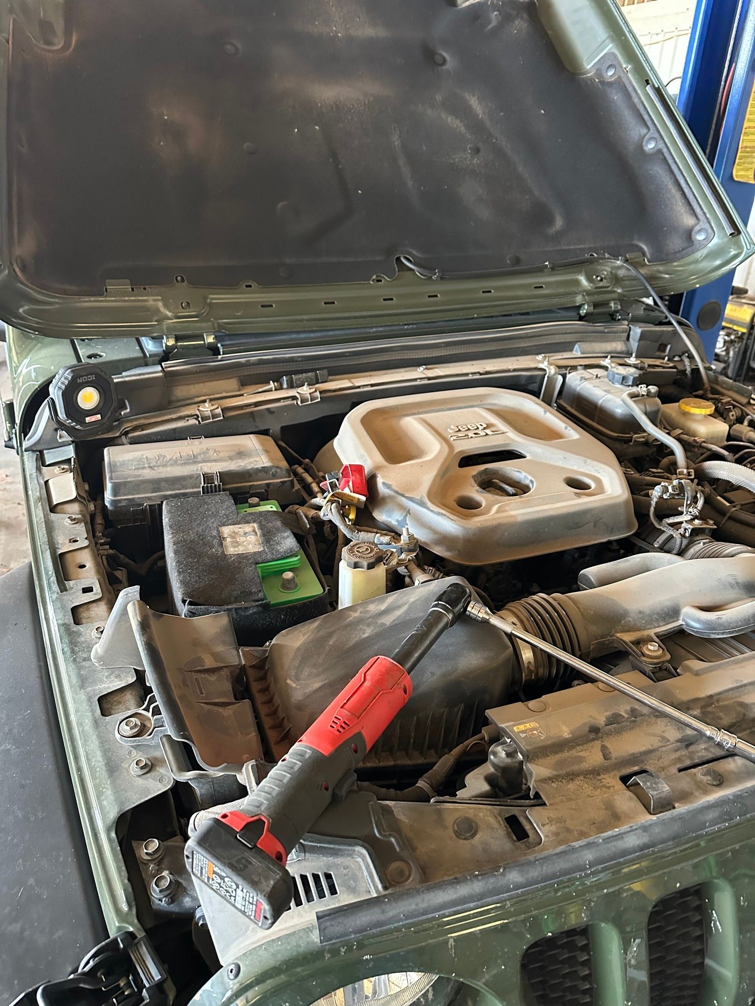 Car hood open, showing a dusty engine bay with a red tool resting on the front support.