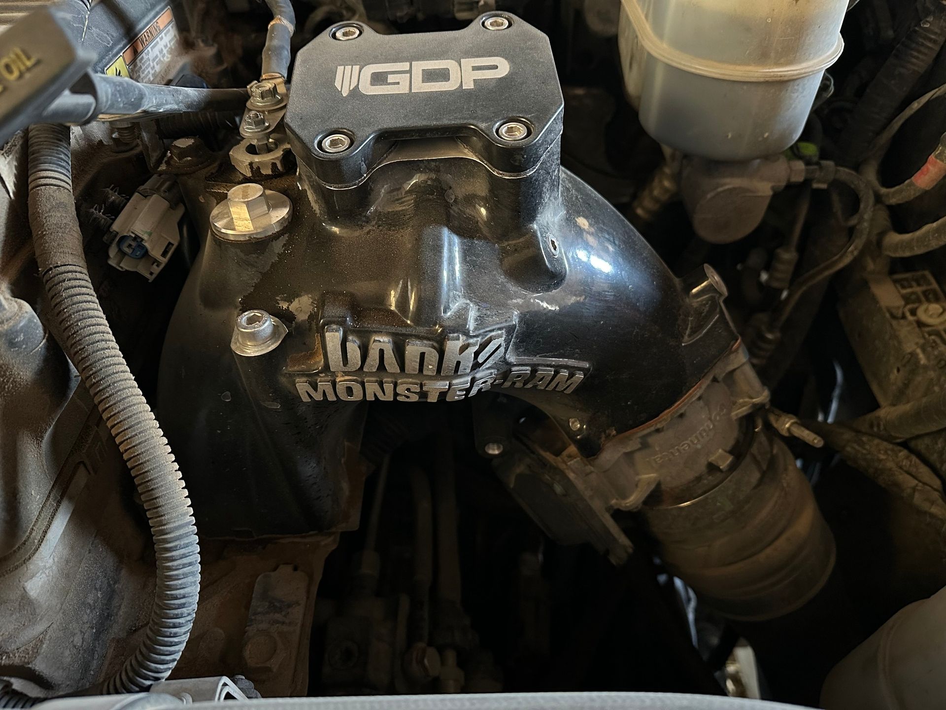 Close-up of a dirty car engine with a black MGDP intake component and hoses around it