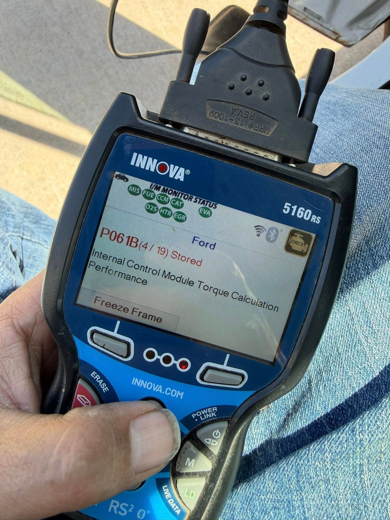 A hand holding a blue handheld meter with a small screen and antenna outdoors.