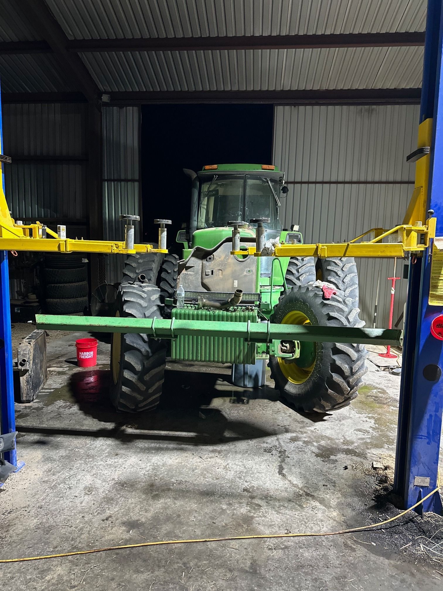 Green tractor with large tires parked inside a metal shed, viewed from the rear.