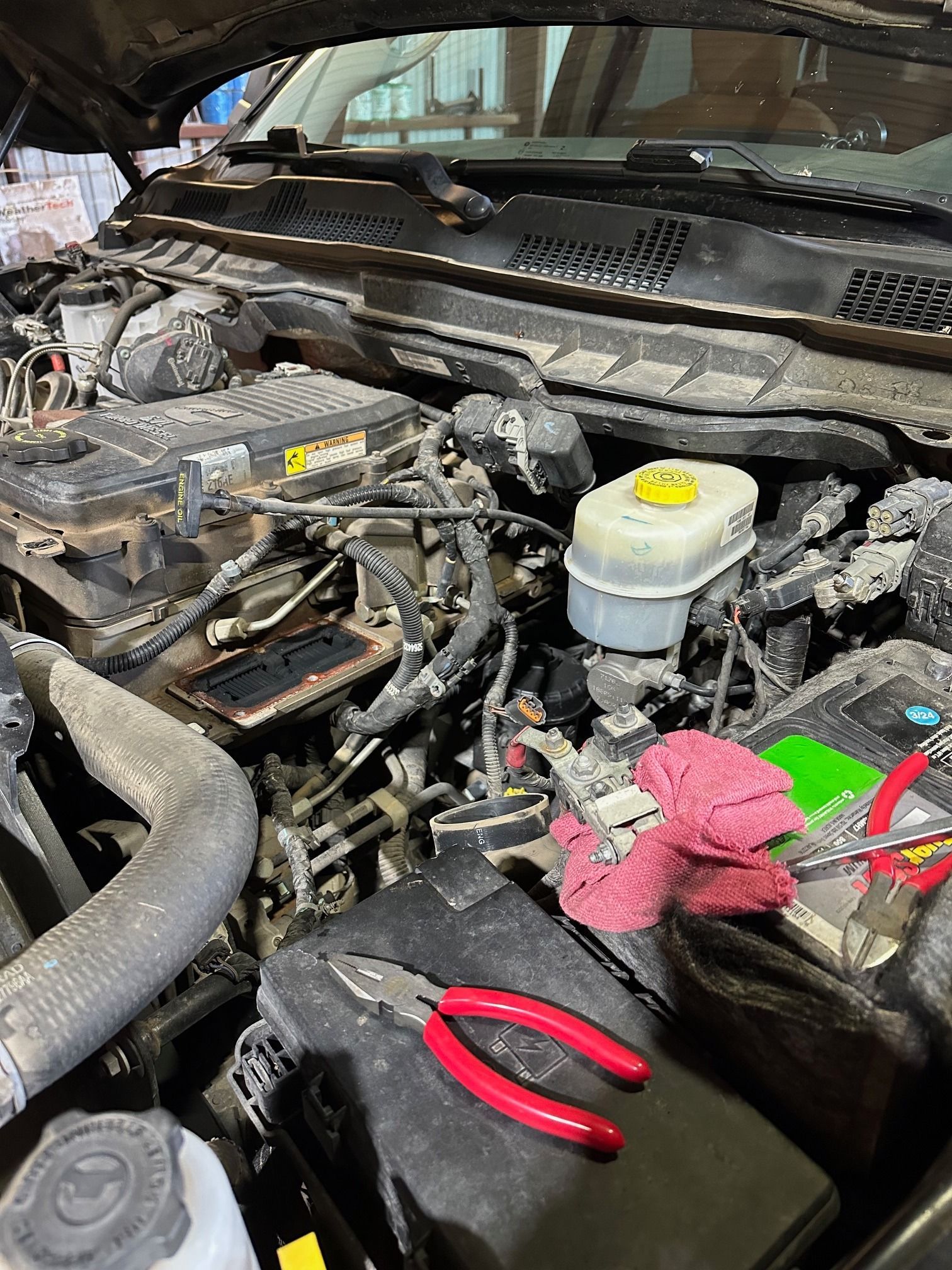 Car engine bay with battery, brake fluid reservoir, tools, and a red rag on the fender