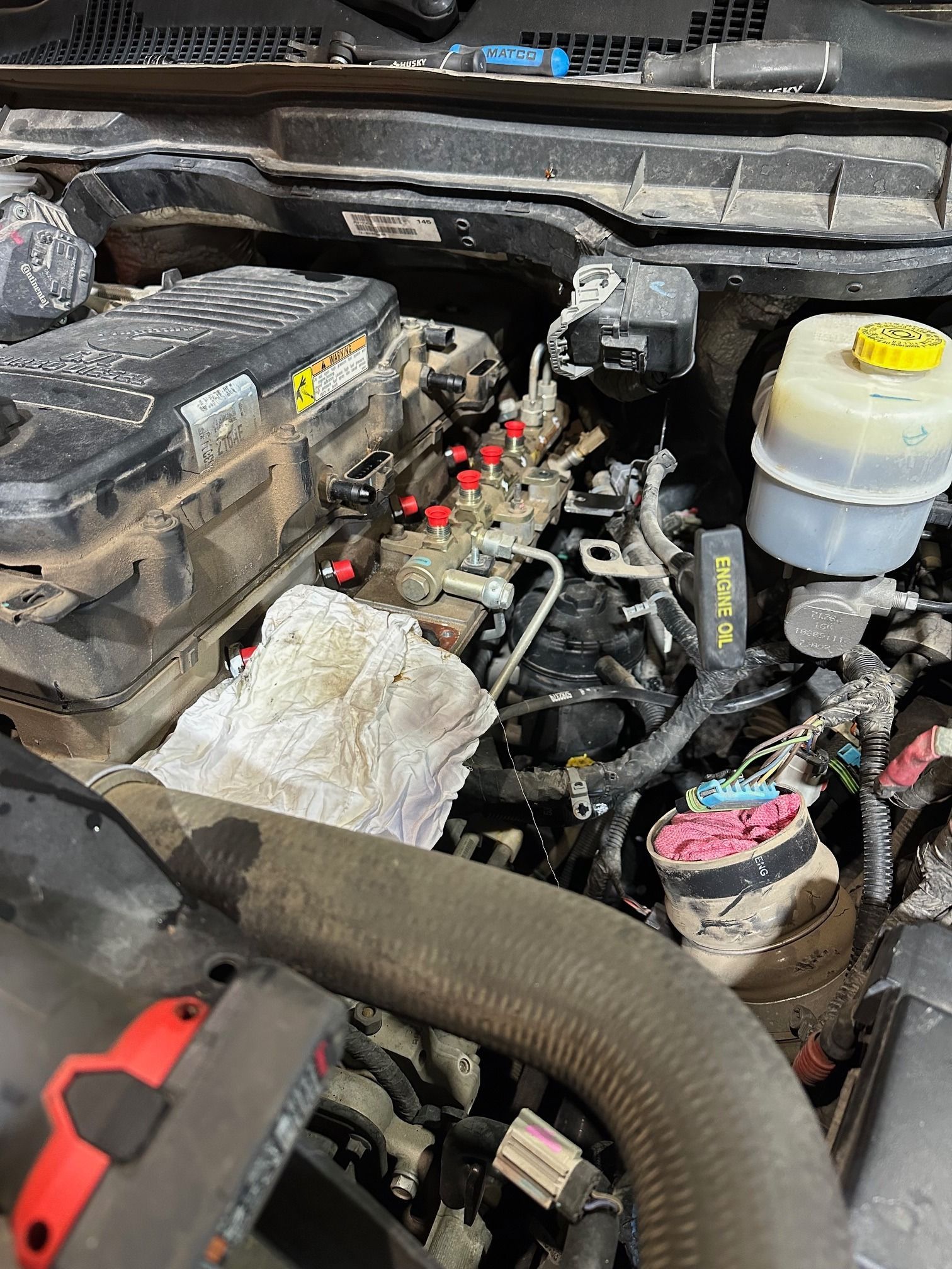 Open car engine bay with exposed components, hoses, and fluid reservoirs under the hood.