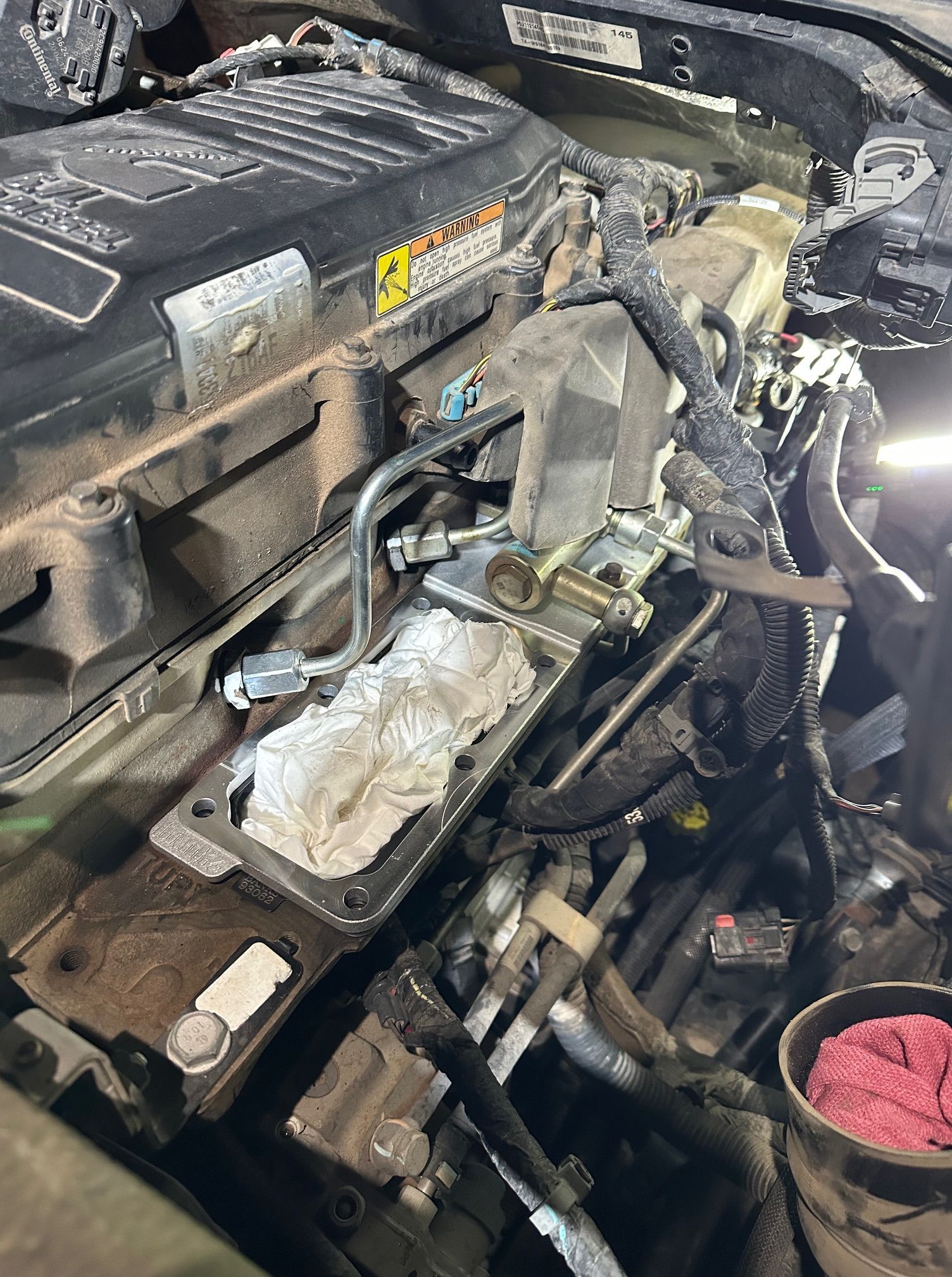 Car engine bay with the engine cover removed, exposing hoses, wires, and mechanical components.