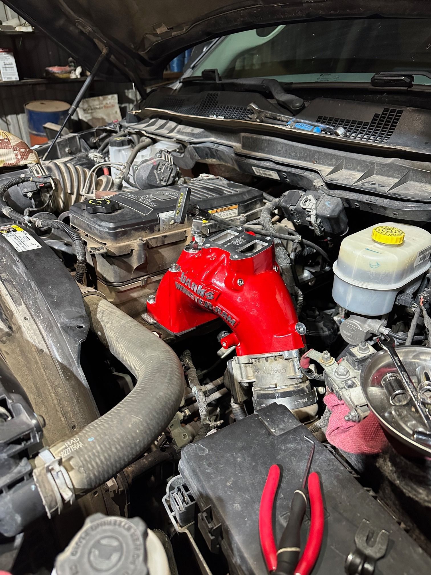 Engine bay with a bright red intake manifold and hoses during car repair.