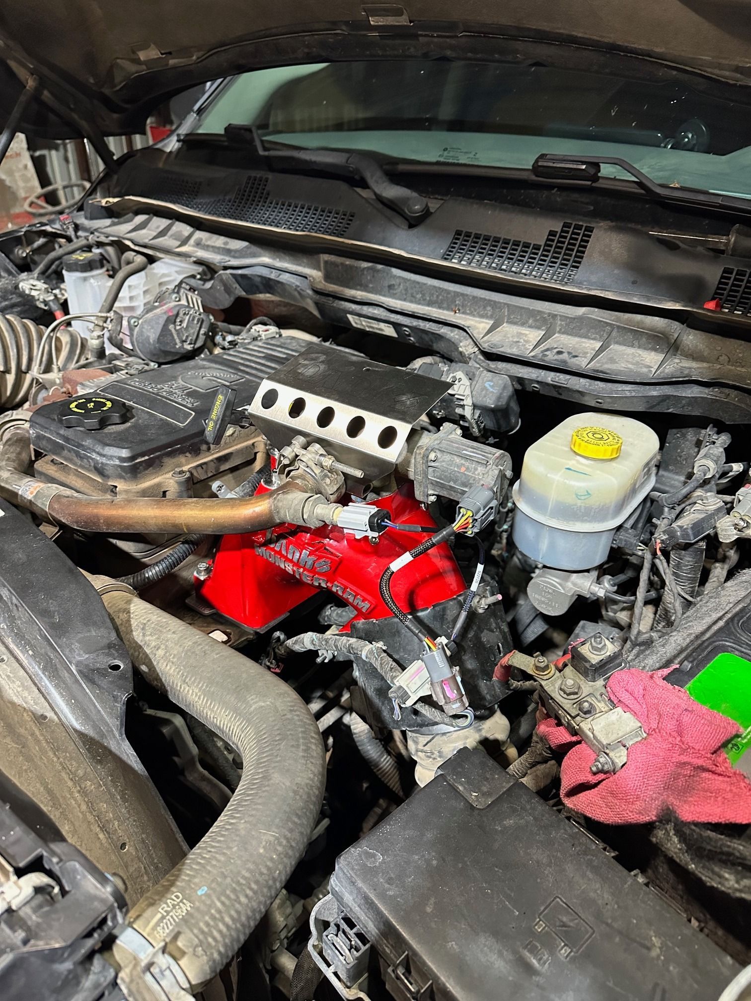 Car engine bay with exposed red engine components and a yellow fluid reservoir under the hood