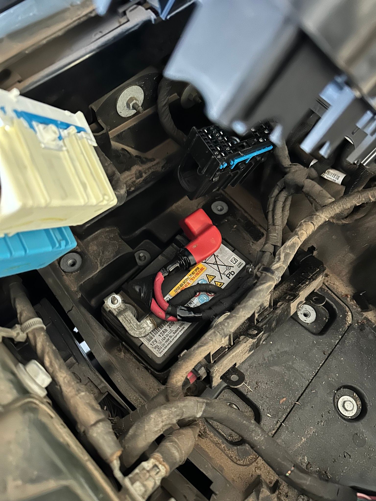 Close-up of a car battery compartment with red and black terminals and wiring under the hood