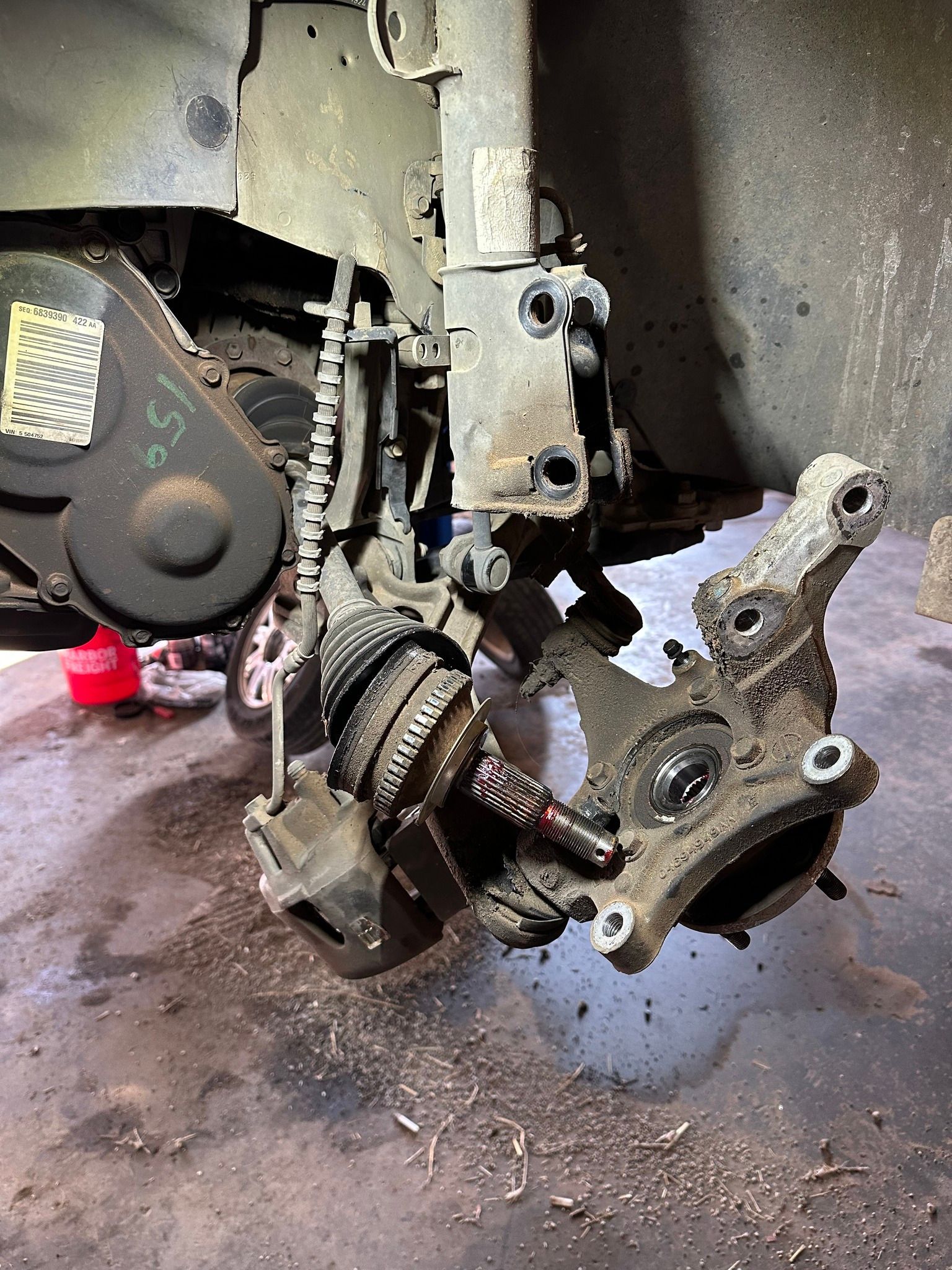 Detached car wheel hub and suspension assembly hanging under a vehicle in a garage, with a coil spring visible.