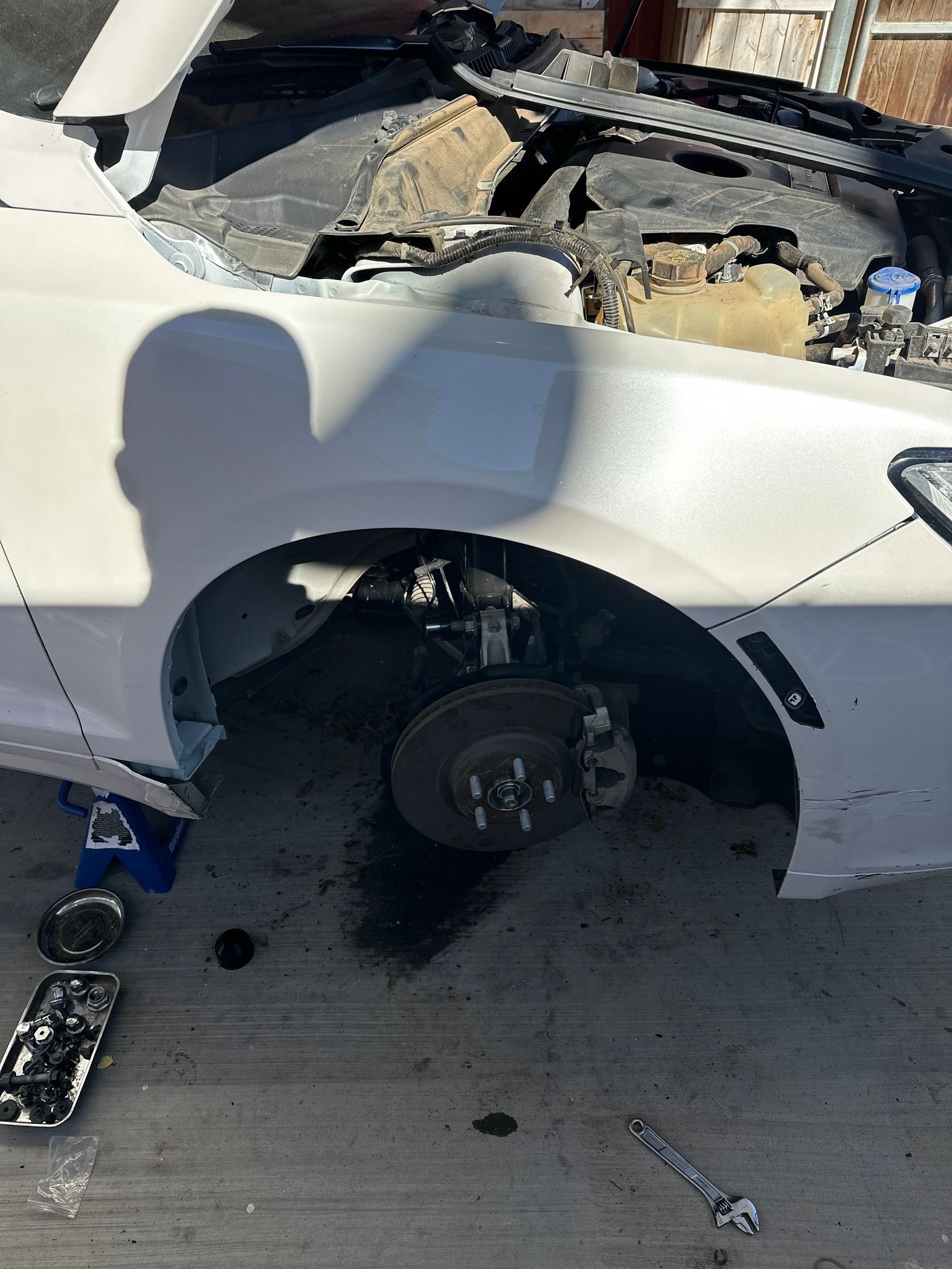 Damaged white car with roof torn open, wheel removed, and debris scattered on the ground.