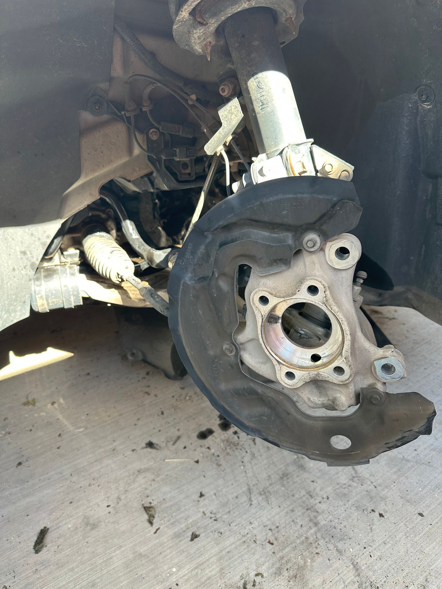 Car wheel removed, exposing brake rotor, hub, and suspension in a garage.