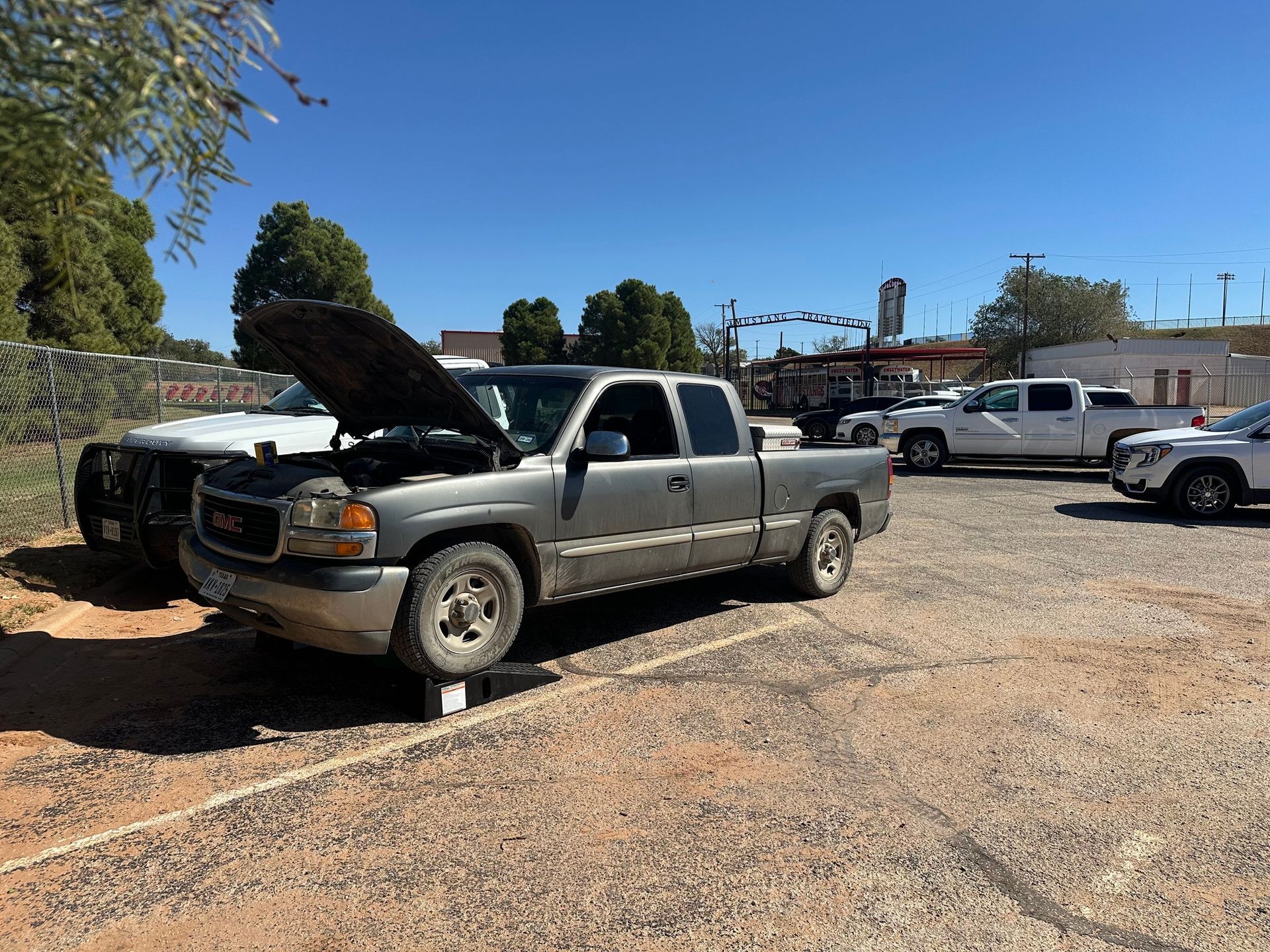 Silver pickup truck with hood open in a gravel parking lot on a sunny day