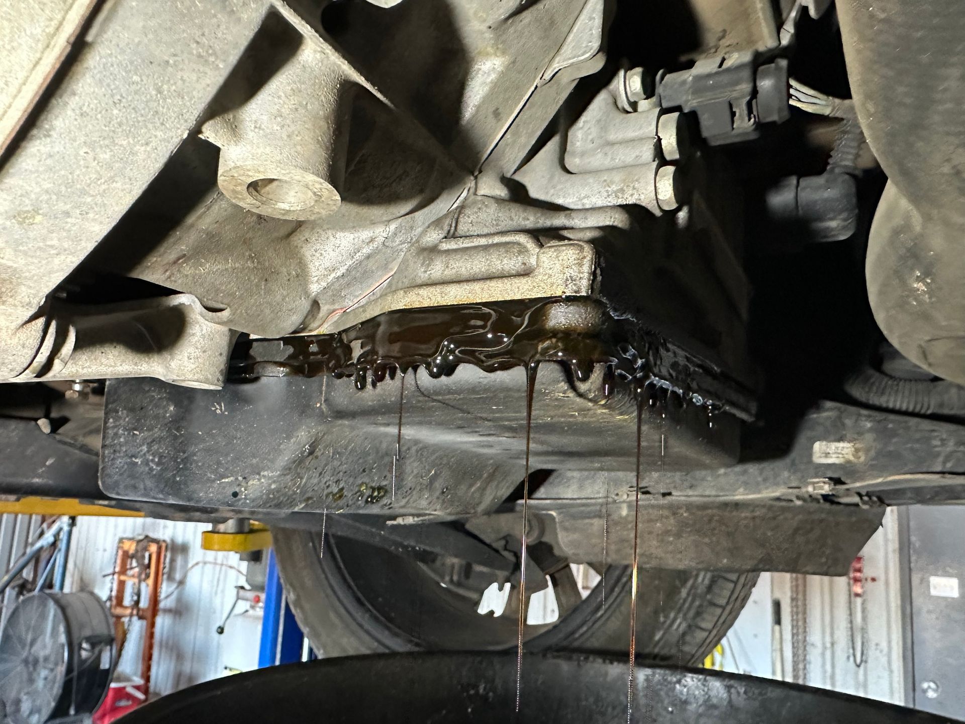 Underside of a car with dark fluid leaking onto the floor in a garage.
