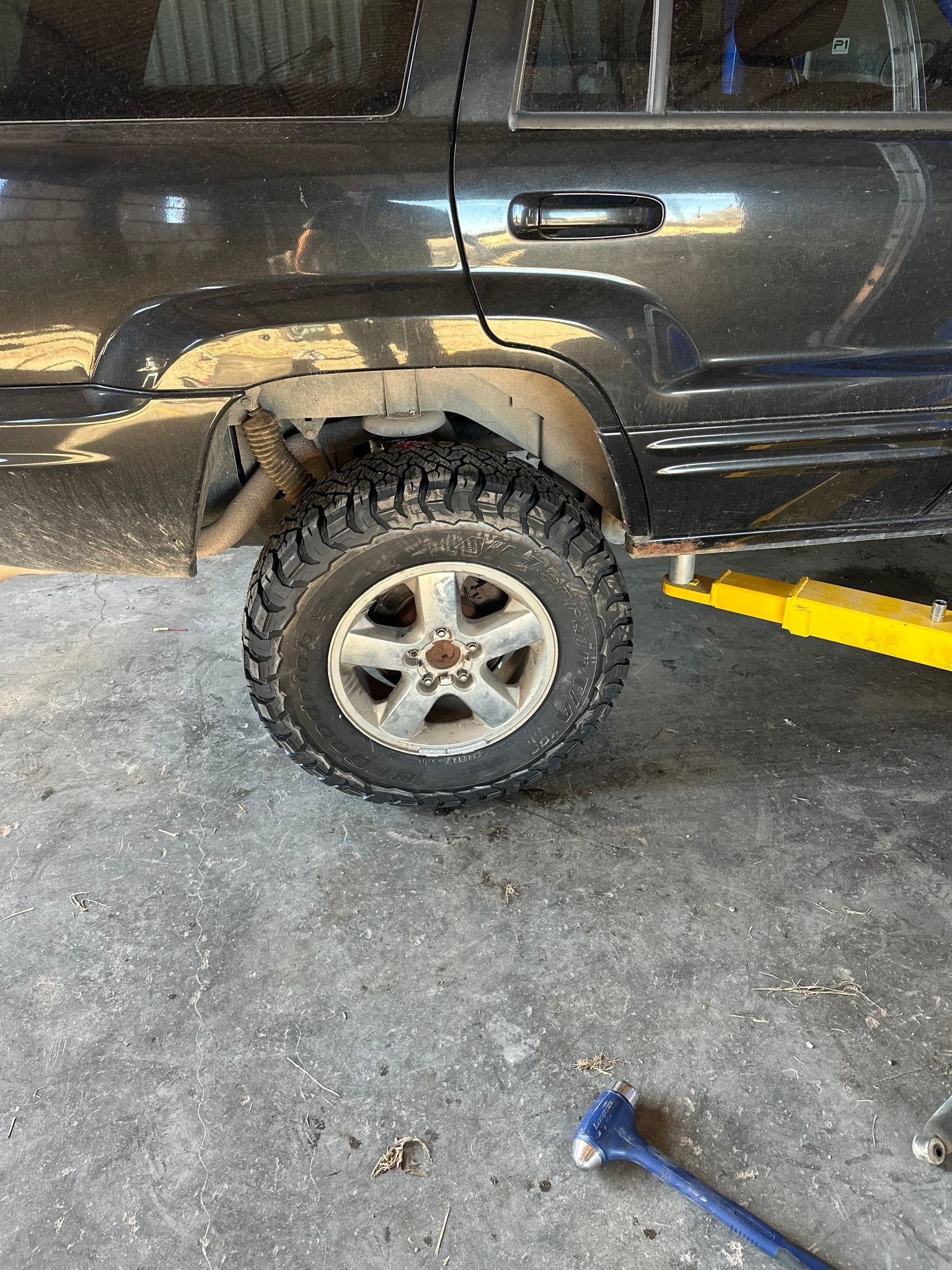 Truck wheel and fender in a garage, with a jack and yellow ramp beneath the vehicle.