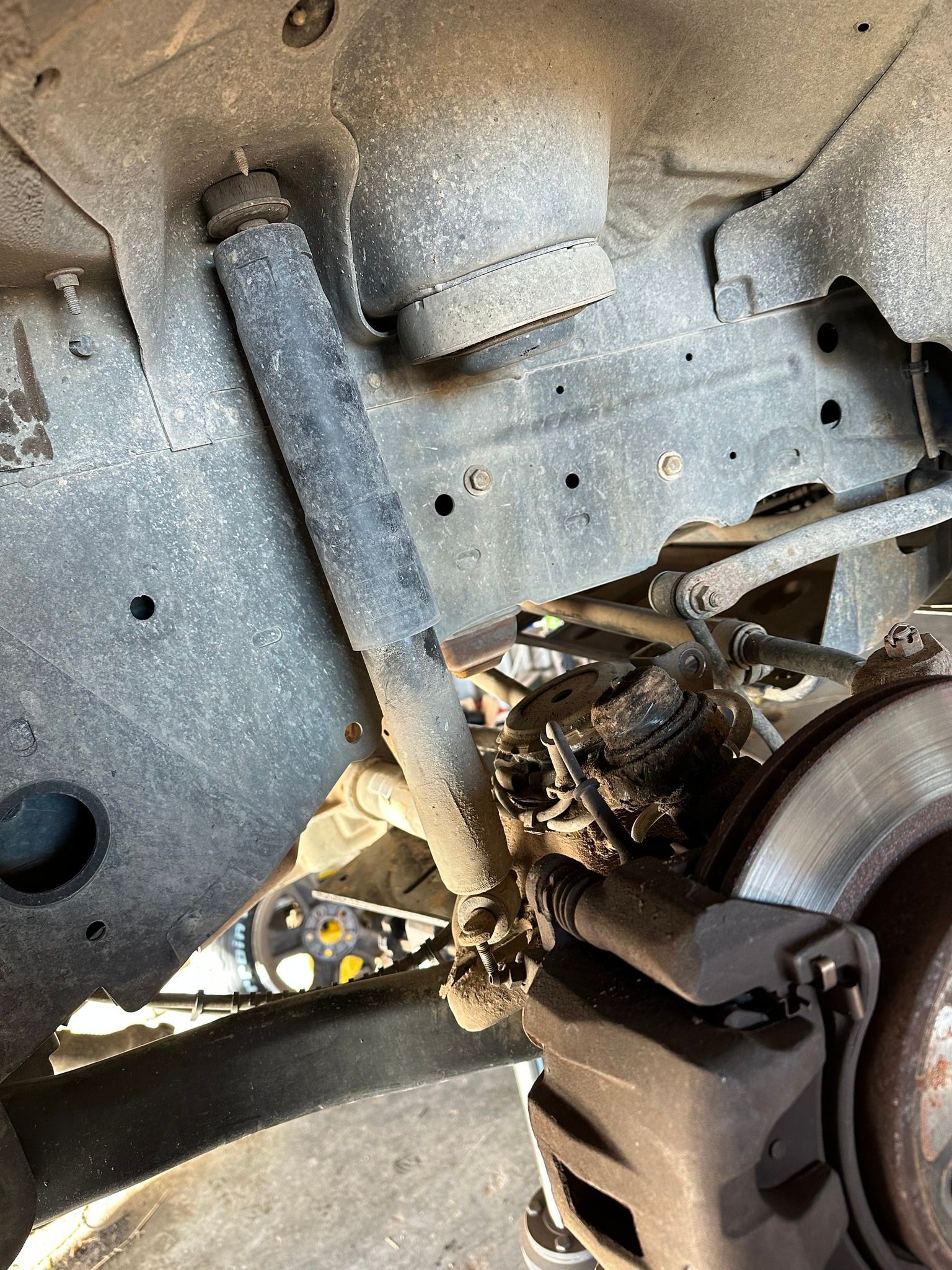 Underbody view of a vehicle’s suspension and wheel area with rust and damaged components