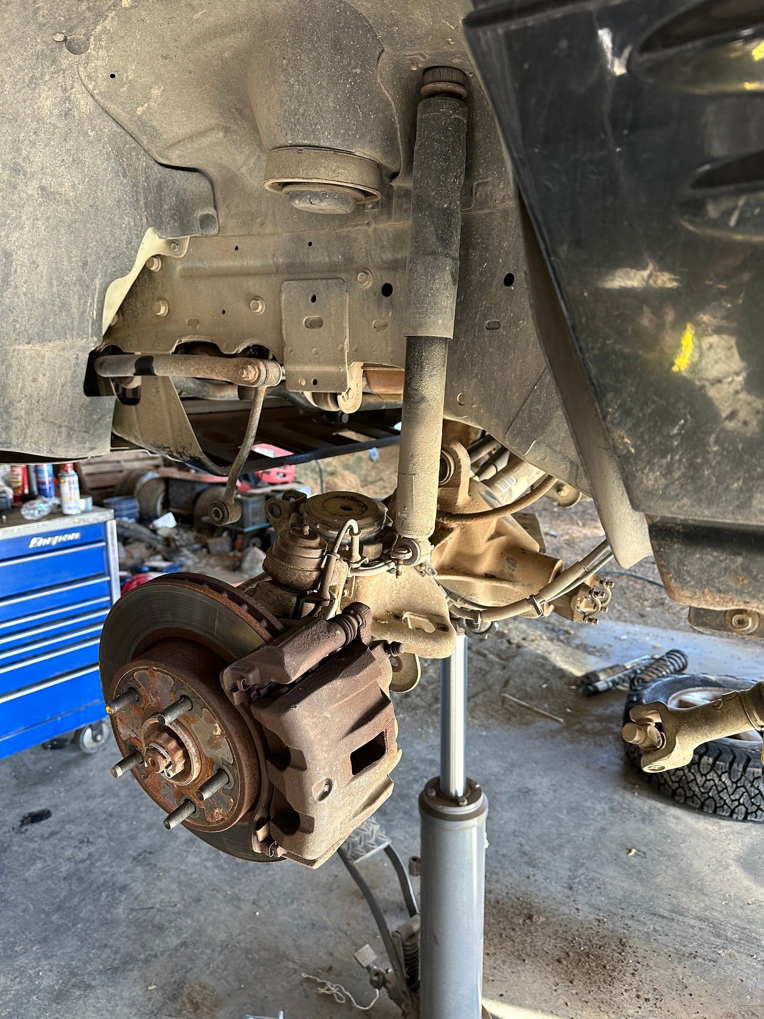 Car wheel and brake assembly raised on a floor jack inside a garage, with the wheel removed.