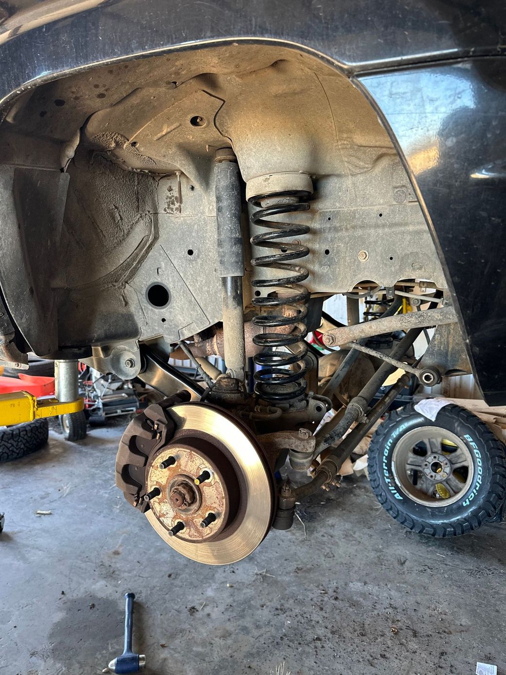 Car wheel removed, exposing suspension and brake assembly inside a lifted vehicle in a garage