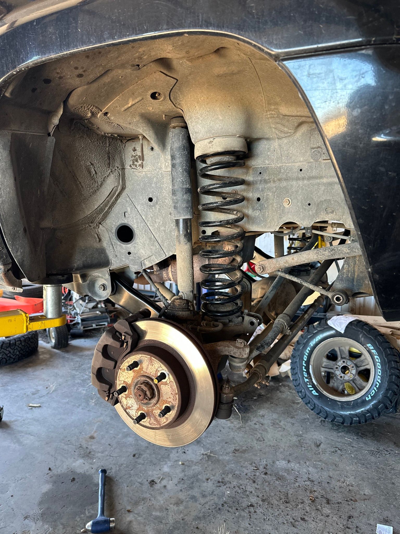 Car wheel removed, exposing suspension and brake assembly inside a lifted vehicle in a garage