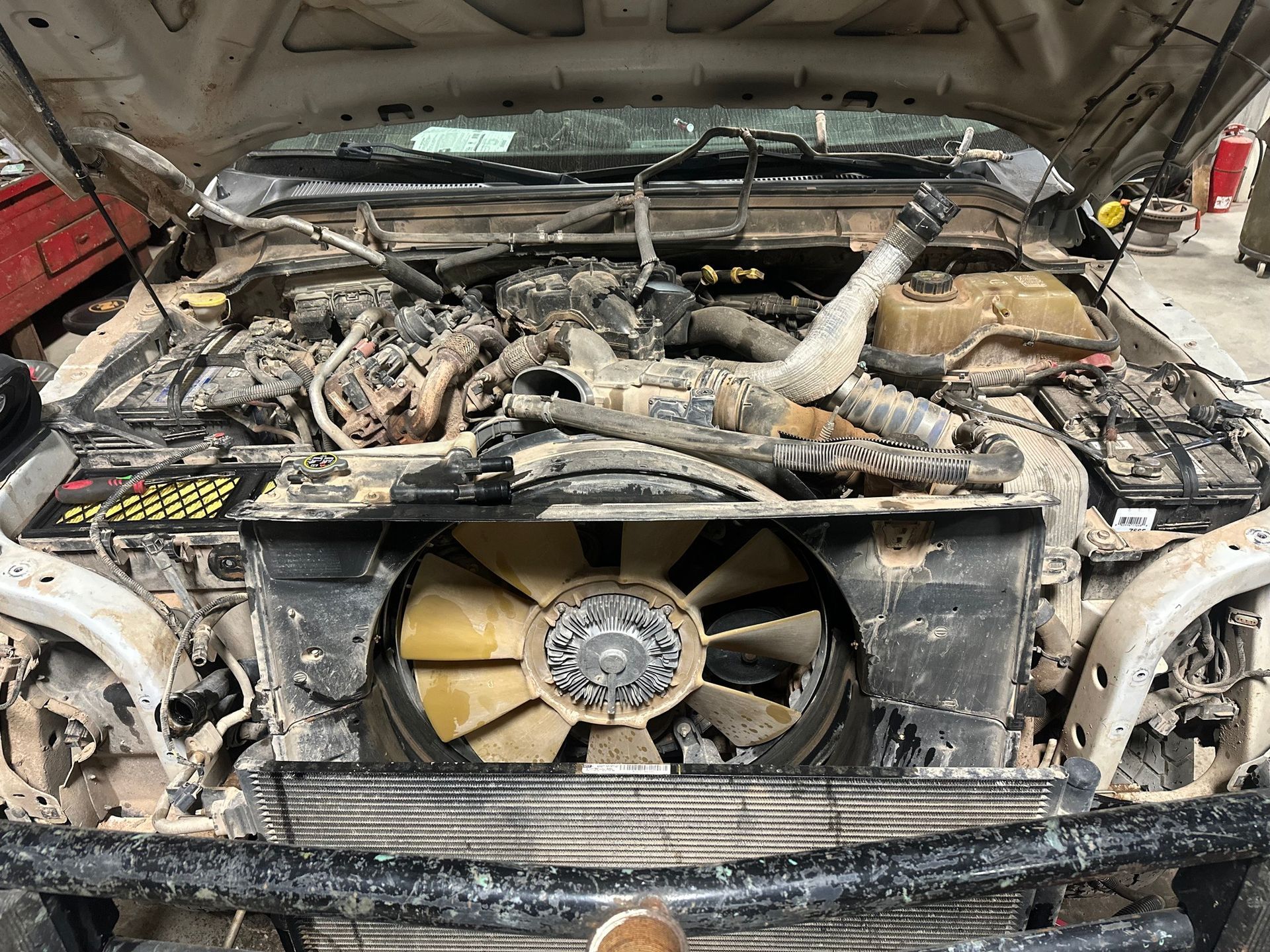 Charred car engine bay with exposed radiator fan and burned wiring in a garage