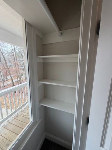 Empty white closet with shelves beside a window and balcony.