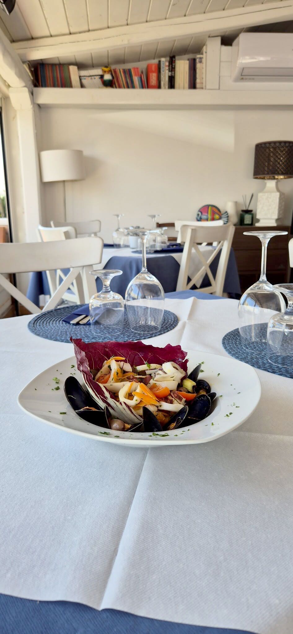 Un tavolo da pranzo bianco con posate blu e bianche e un piatto da dessert in una stanza luminosa.