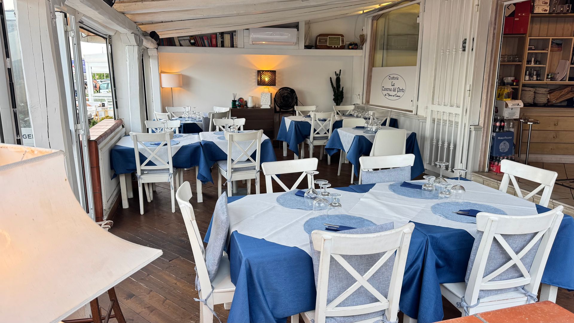 Sala da pranzo luminosa del ristorante con sedie bianche e tovaglie blu, apparecchiata per gli ospiti.