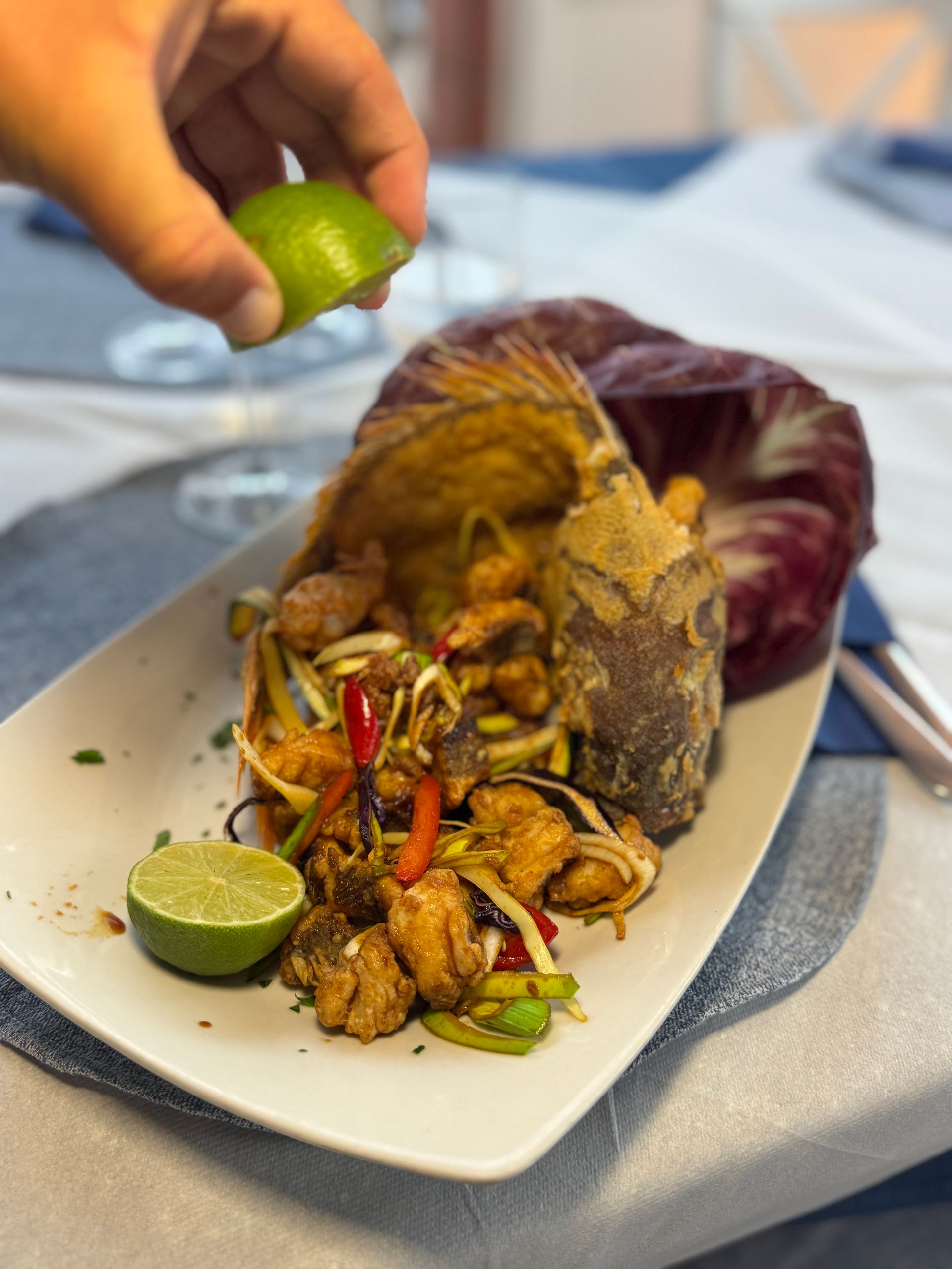 Spremere a mano il lime su un piatto di frutti di mare su un piatto bianco con peperoni e cavolo come guarnizione.