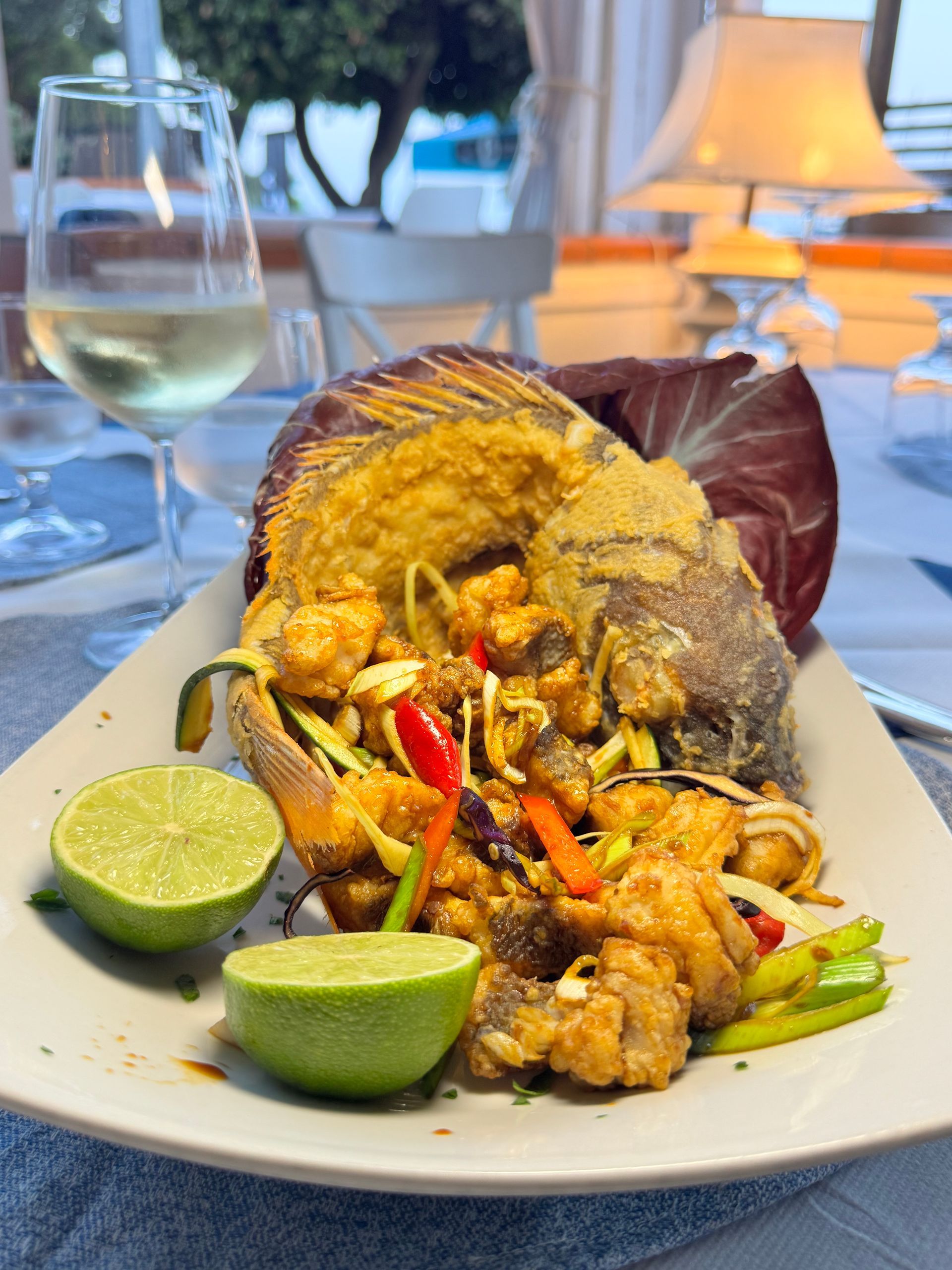 Piatto di frutti di mare con spicchi di lime su un tavolo, con un bicchiere di vino bianco sullo sfondo.