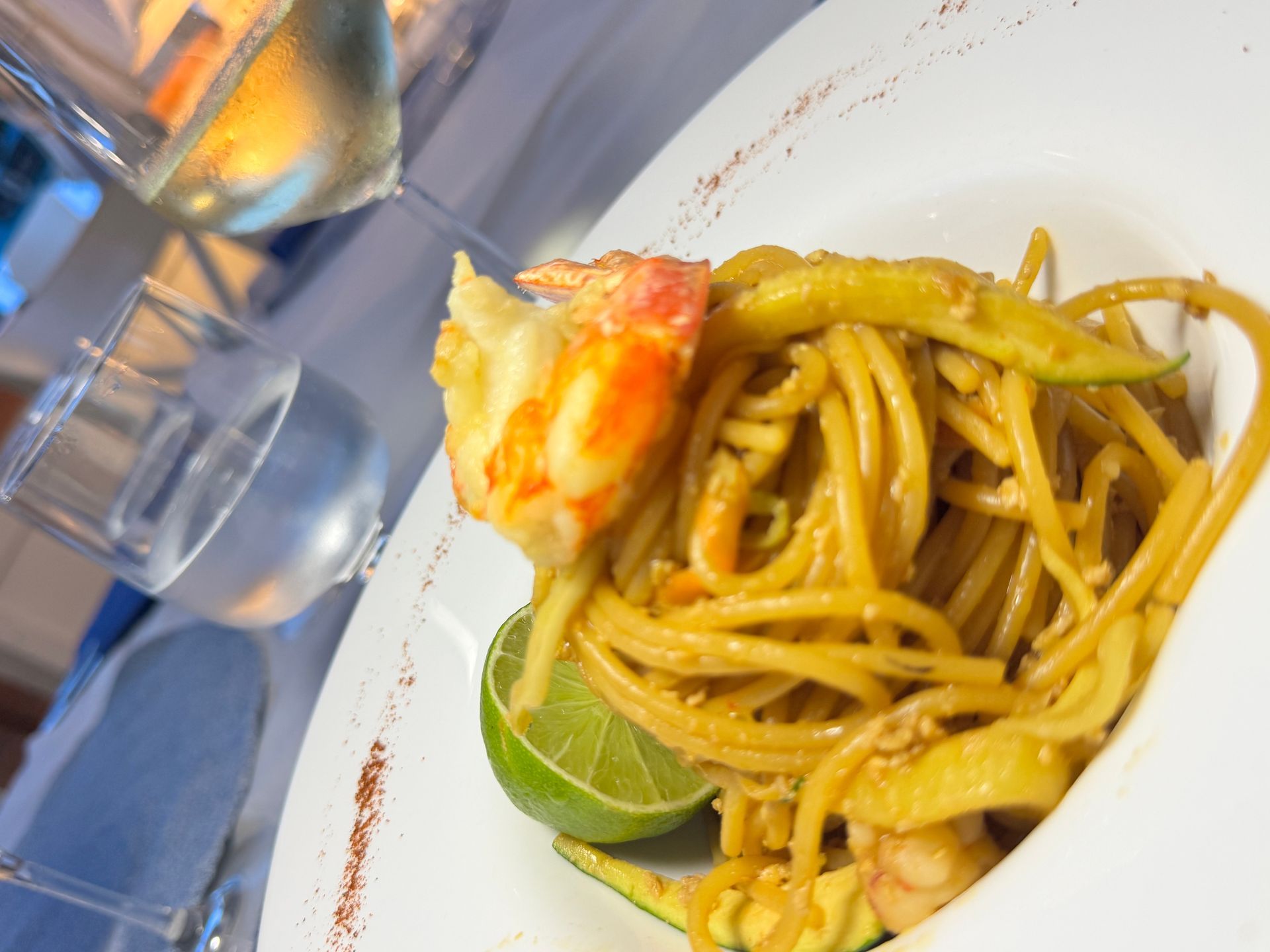 Primo piano di pasta con spicchio di lime e frutti di mare in una ciotola bianca su un tavolo vicino a un bicchiere d'acqua