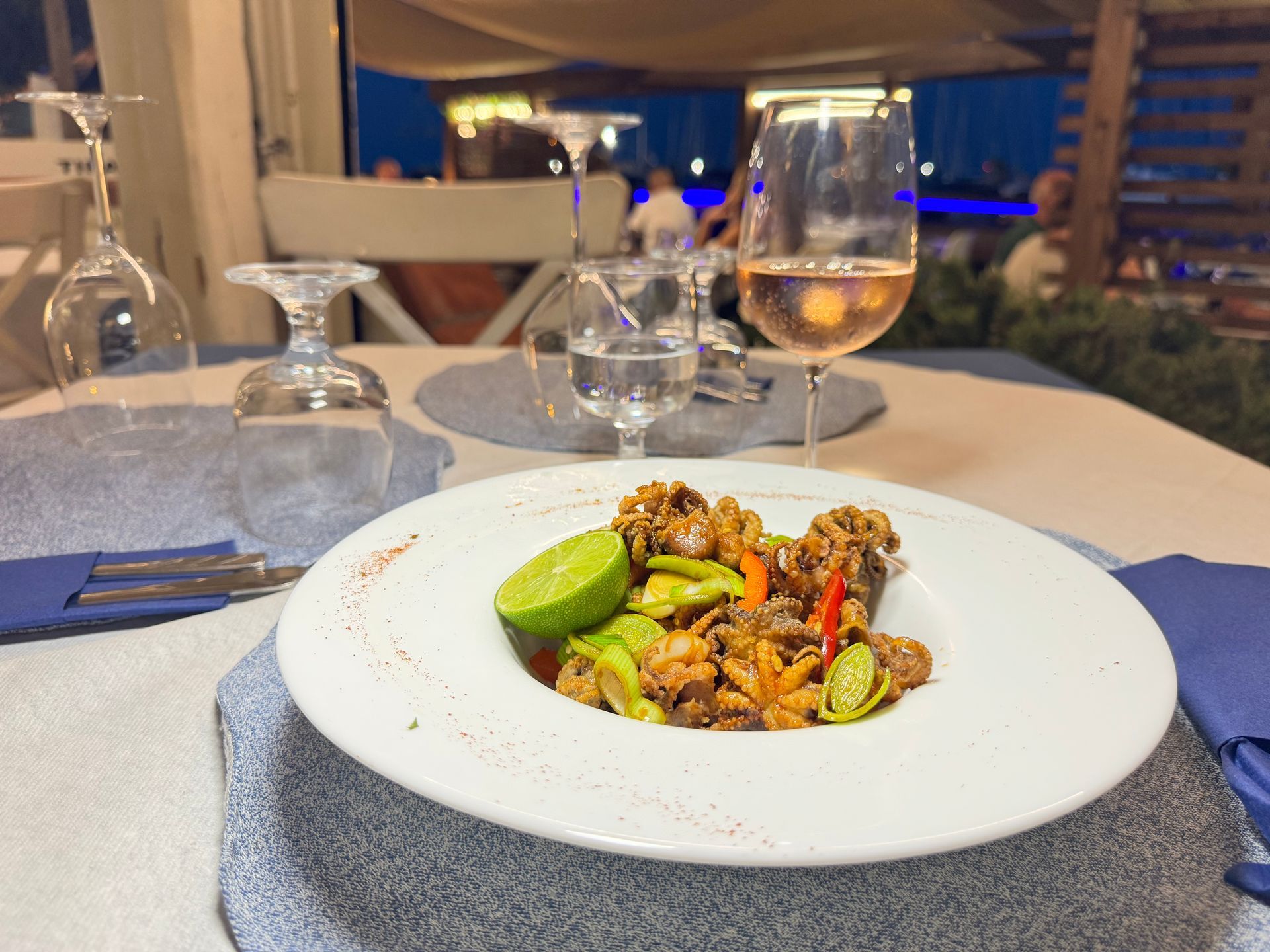 Un pasto gourmet servito su una tovaglia bianca a un tavolo di ristorante illuminato da candele, con calici di vino.