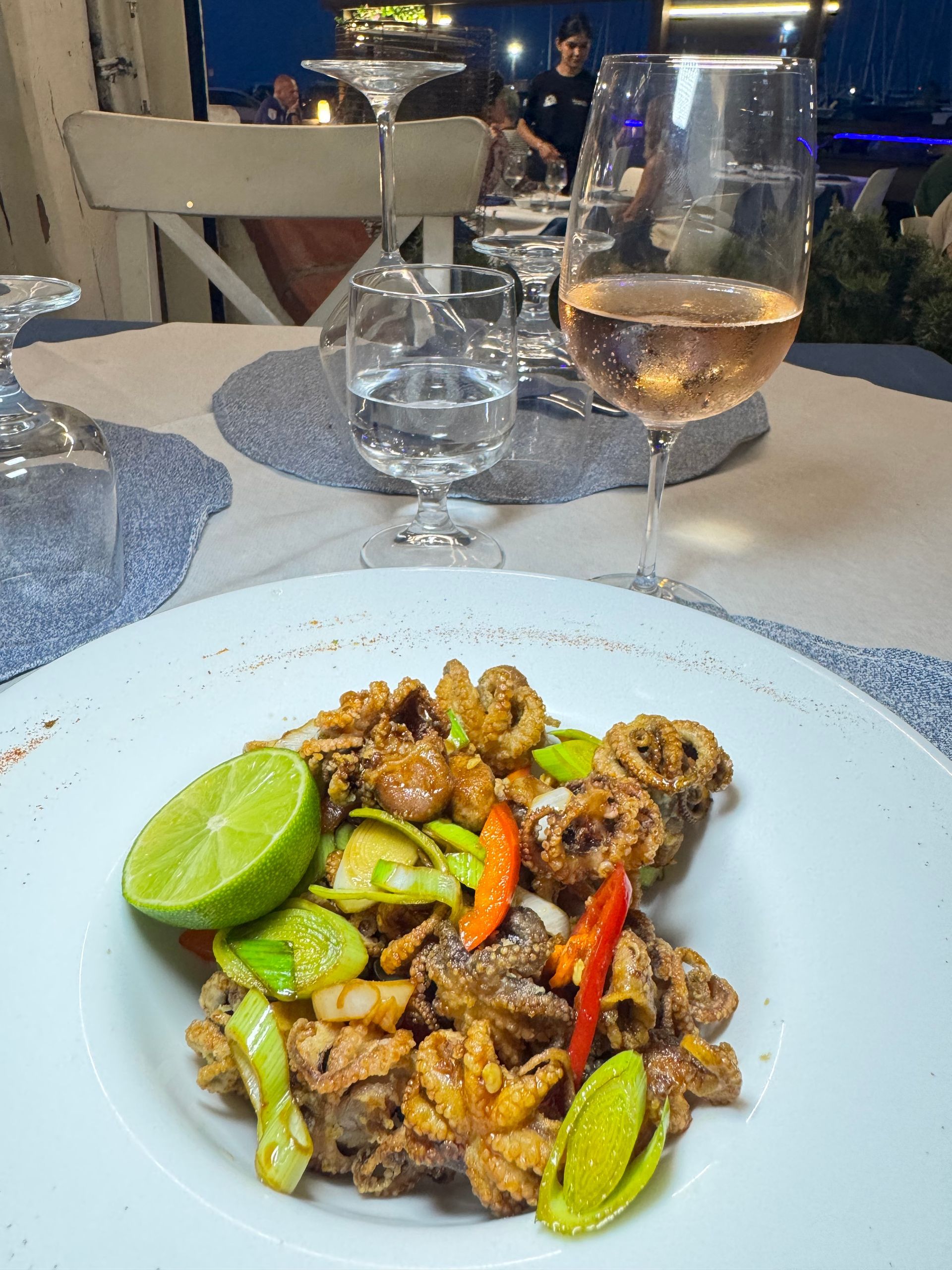 Un piatto di carne saltata in padella e piccante con spicchi di lime su un tavolo di ristorante, con bicchieri d'acqua e di vino nelle vicinanze.
