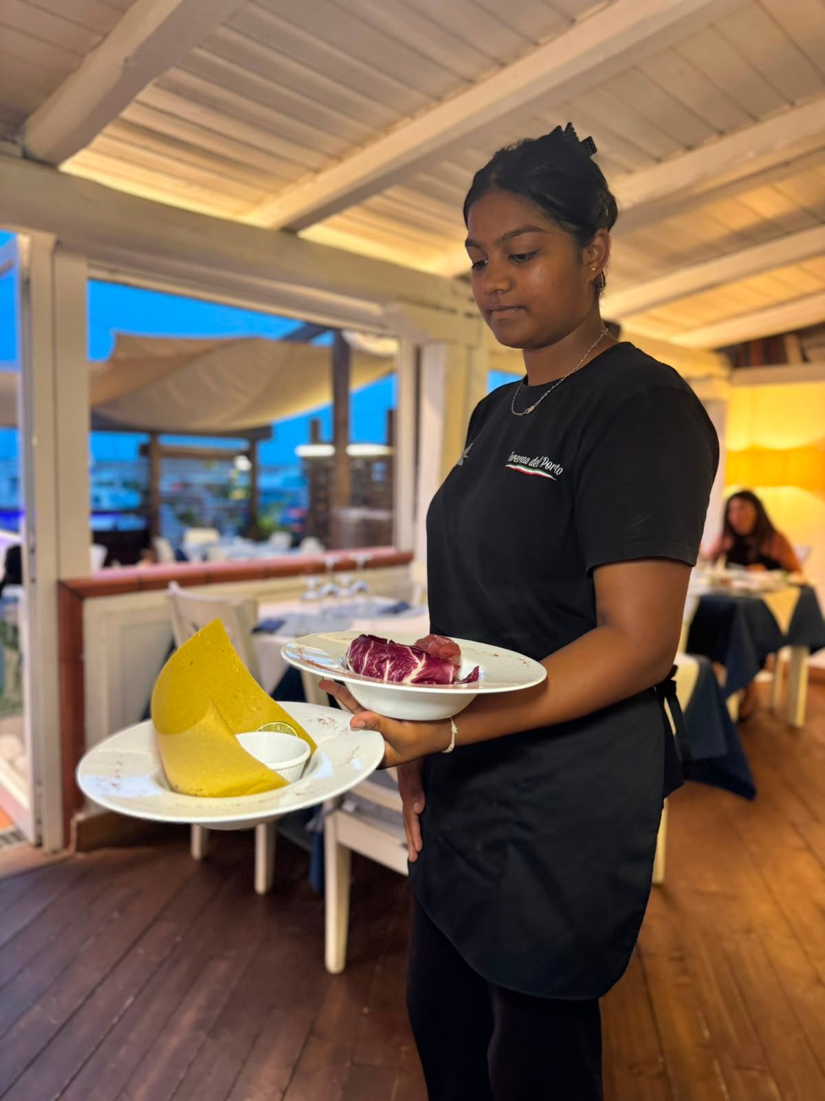 Cameriera che porta dei piatti da dessert in un ristorante, uno con una fetta di torta gialla e uno con un dessert rosso.