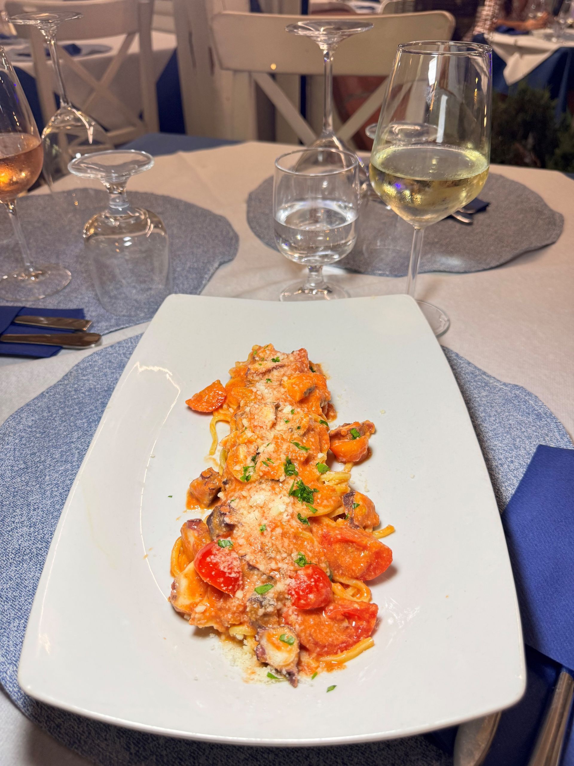 Piatto di pasta con pomodorini ciliegino su un piatto bianco al tavolo di un ristorante, con bicchieri da vino.