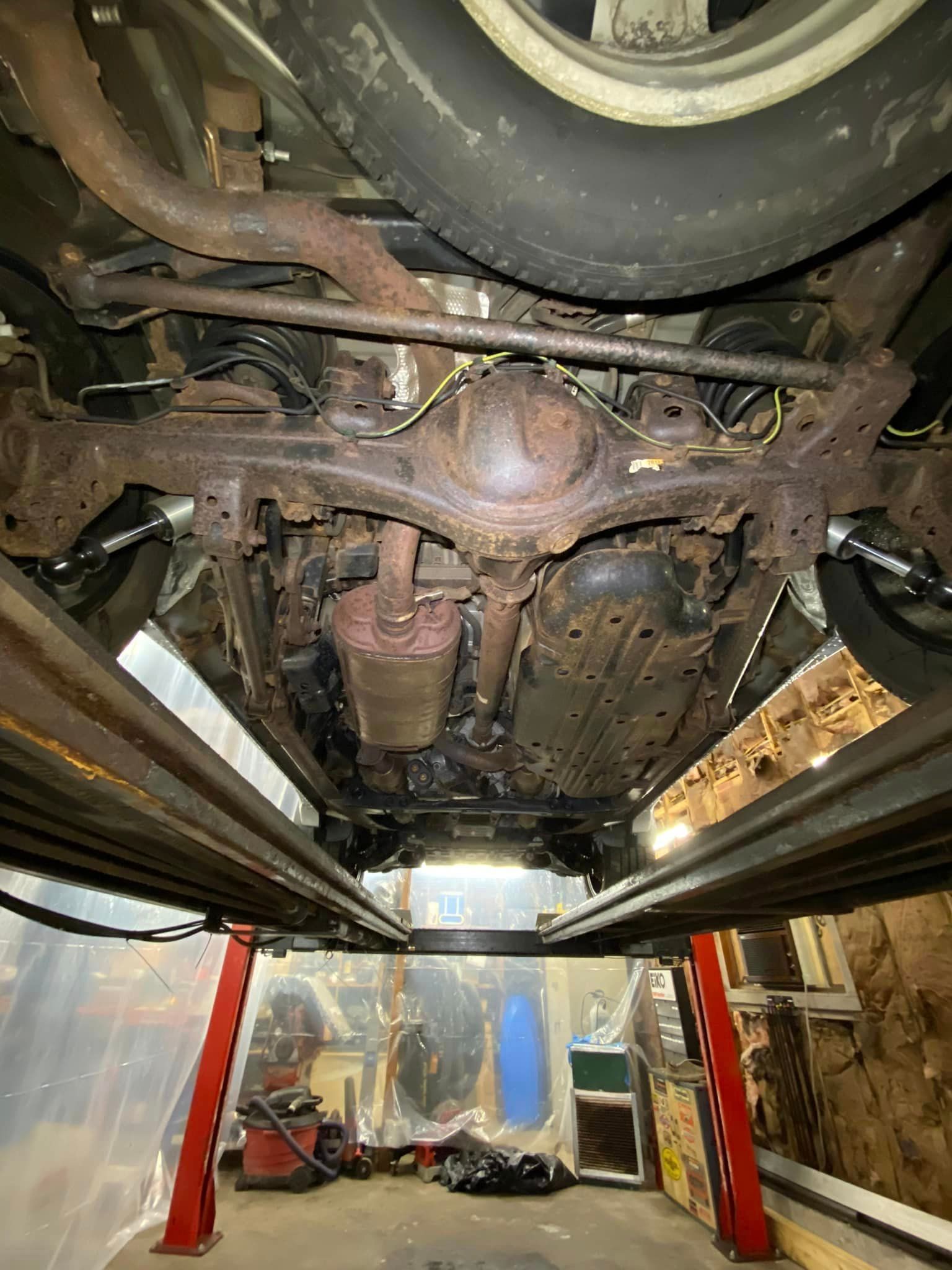 The underside of a car is sitting on a lift in a garage.