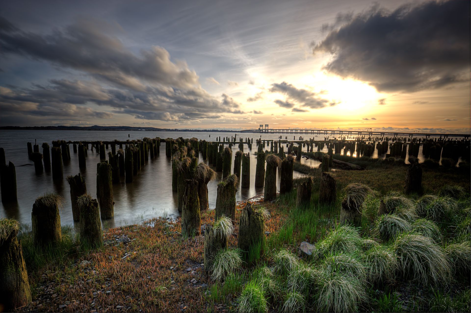 A sunset over a body of water with a row of wooden posts in the foreground.