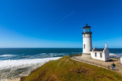 A lighthouse is sitting on top of a grassy hill overlooking the ocean.