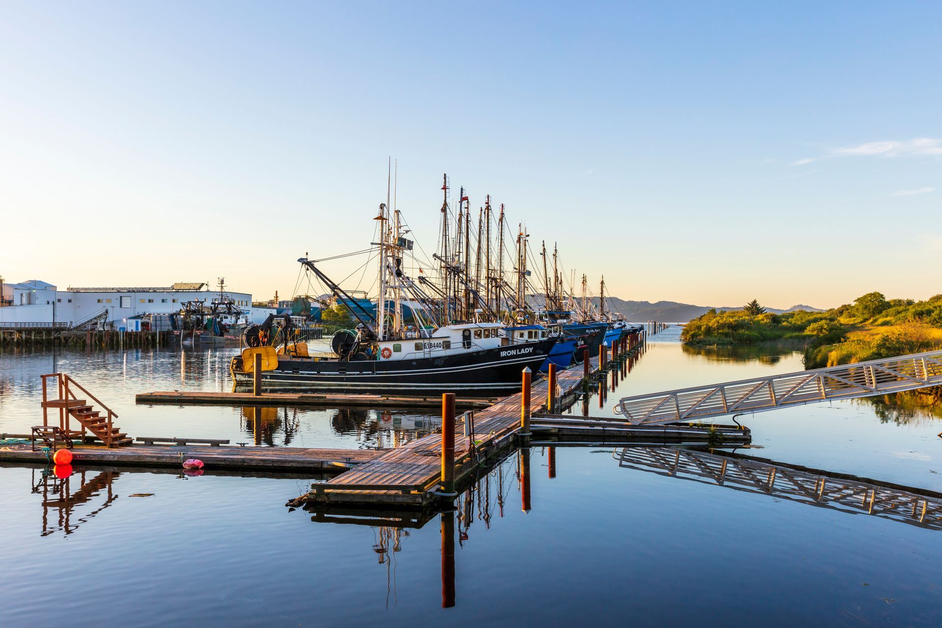 A row of boats are docked at a dock in a harbor.