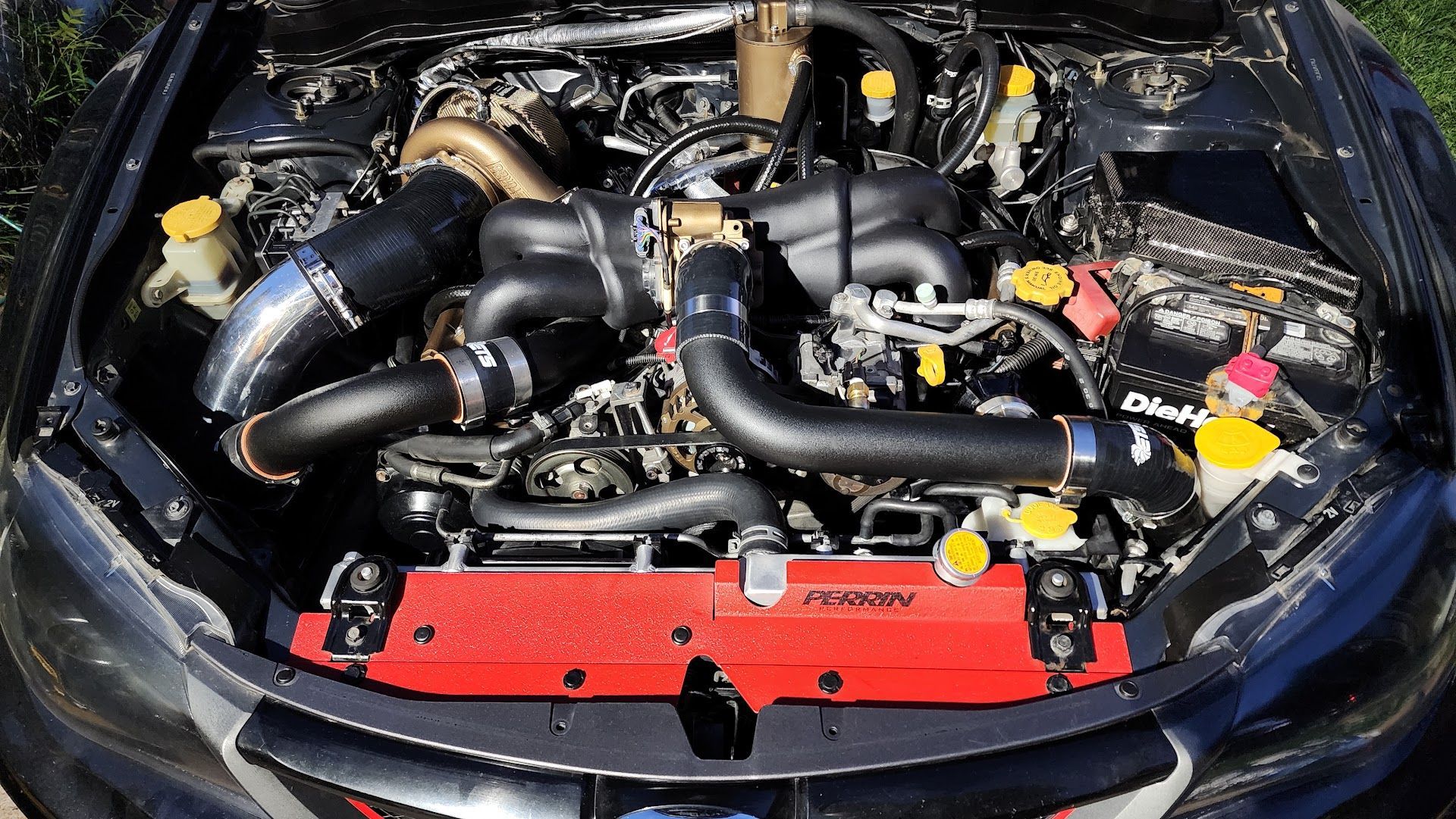 Top-down view of a modified Subaru engine bay with a red radiator, black intake piping, and a large turbocharger. | Teter Automotive