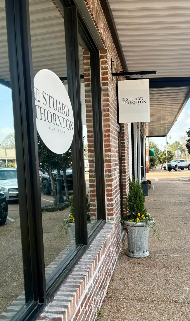 Storefront with brick facade, large windows, and a round sign under a covered sidewalk.