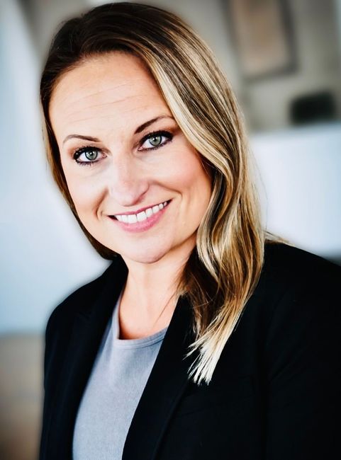 Portrait of a smiling woman in a black blazer and gray top against a blurred office background