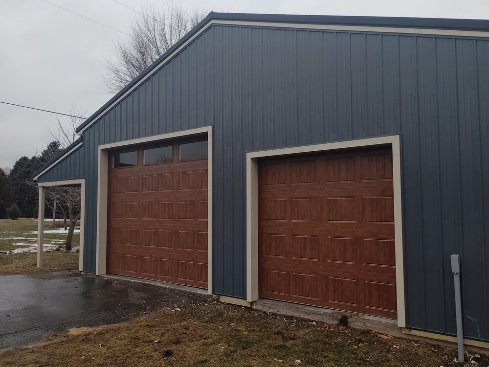 Two-car garage with gray siding and brown wooden doors on a wet driveway