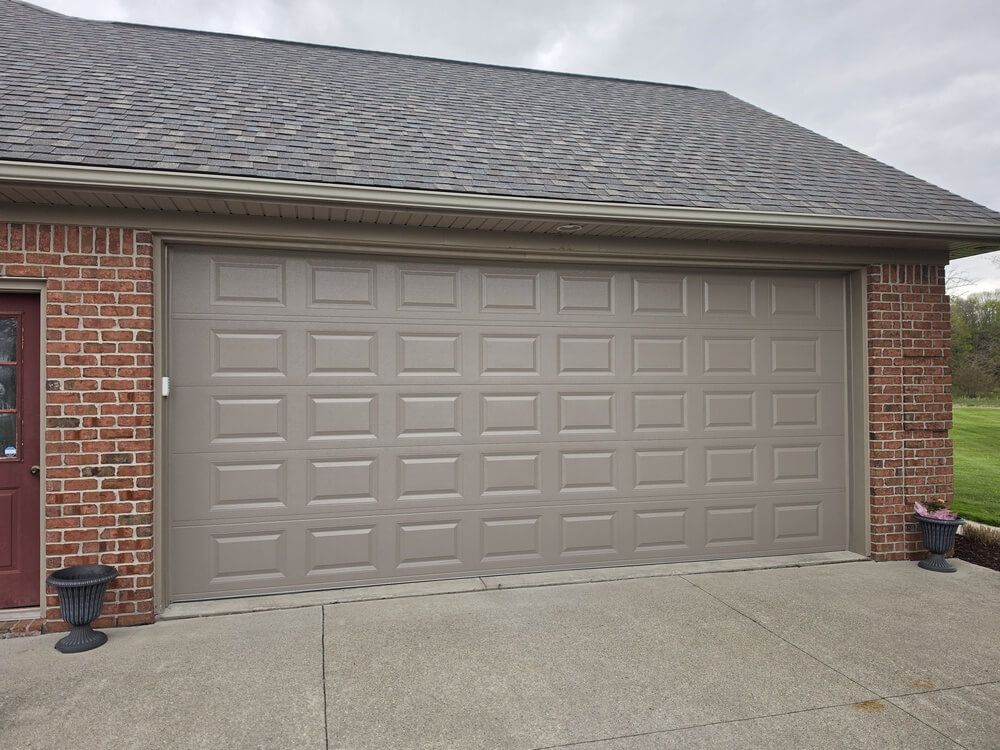 Two-car beige garage door on a brick house with a concrete driveway and small potted plants