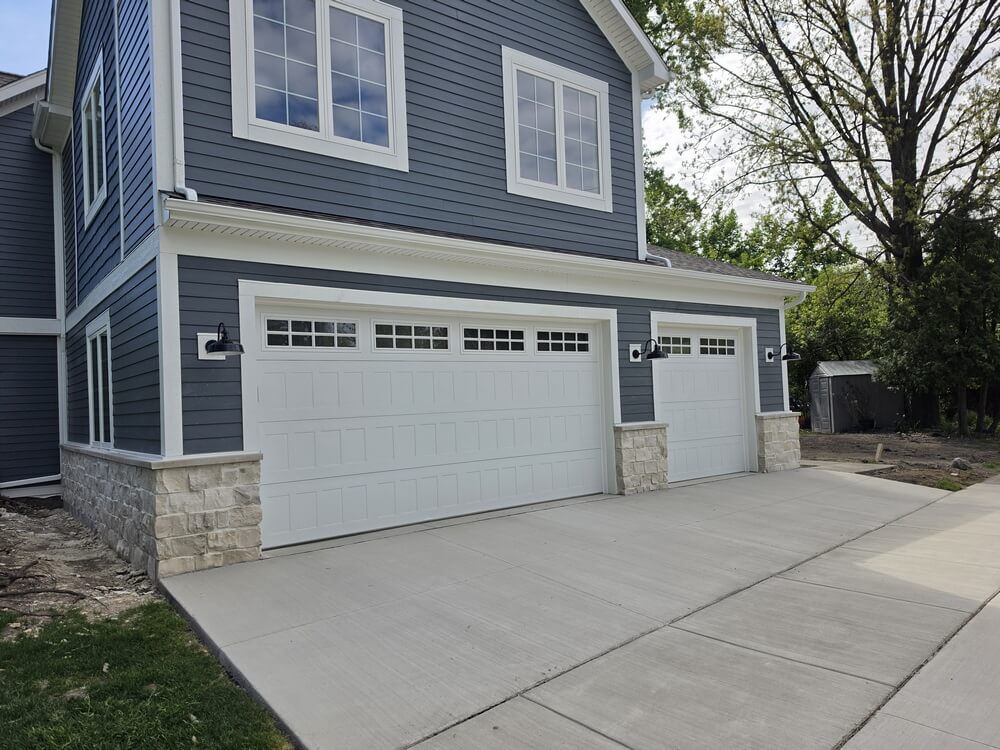Blue two-story house with white garage doors and a wide concrete driveway.