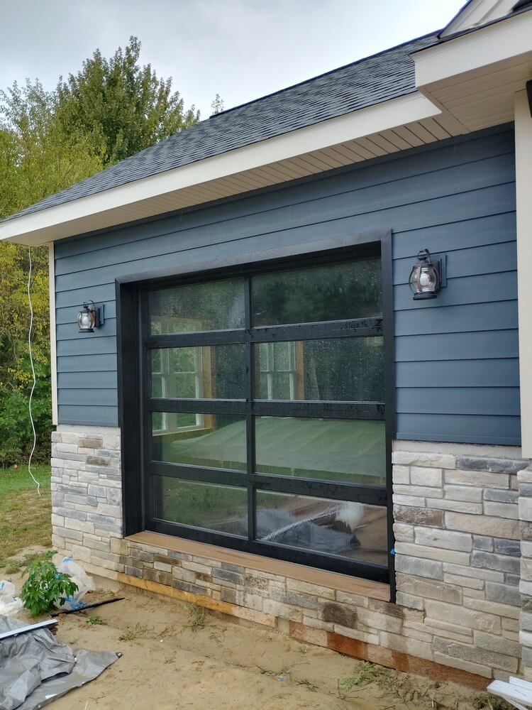 Blue siding house exterior with large black-framed window and stone veneer base