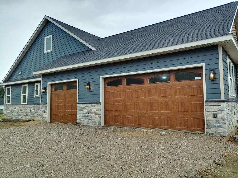 Blue house with stone accents, wood garage doors, and a gravel driveway
