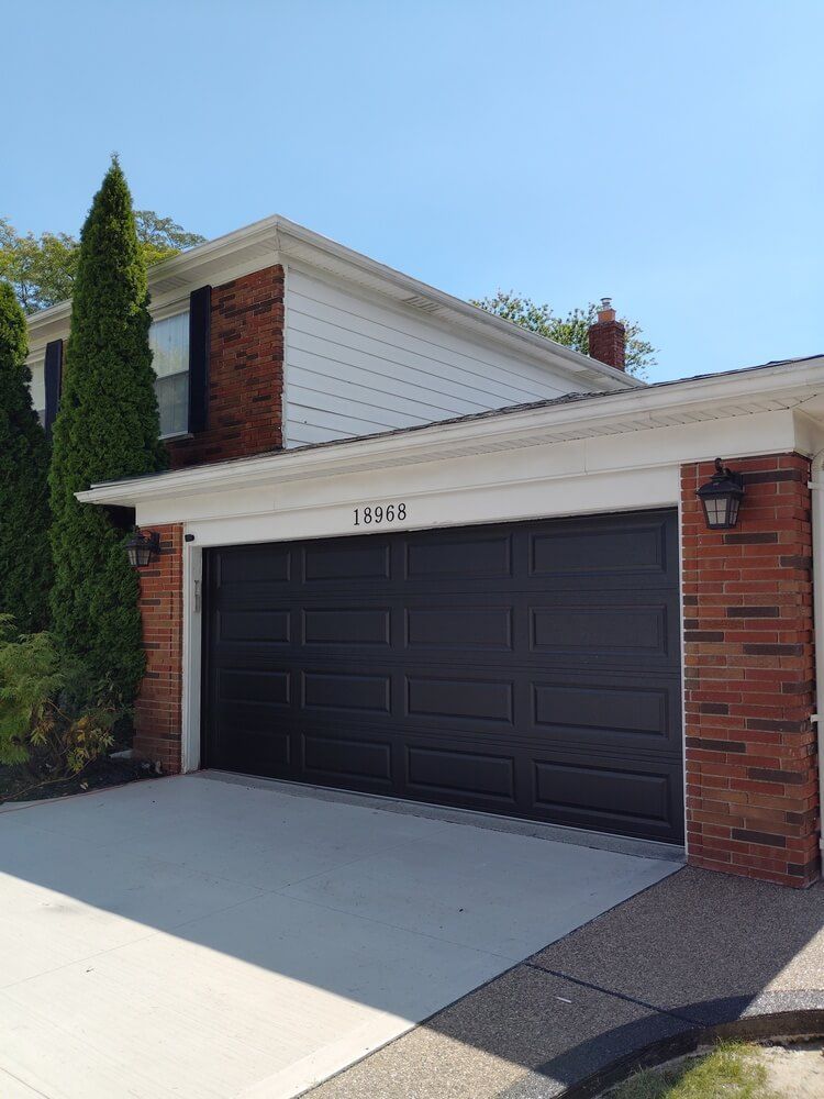 Suburban house with a black double garage door, brick trim, and a driveway under a blue sky