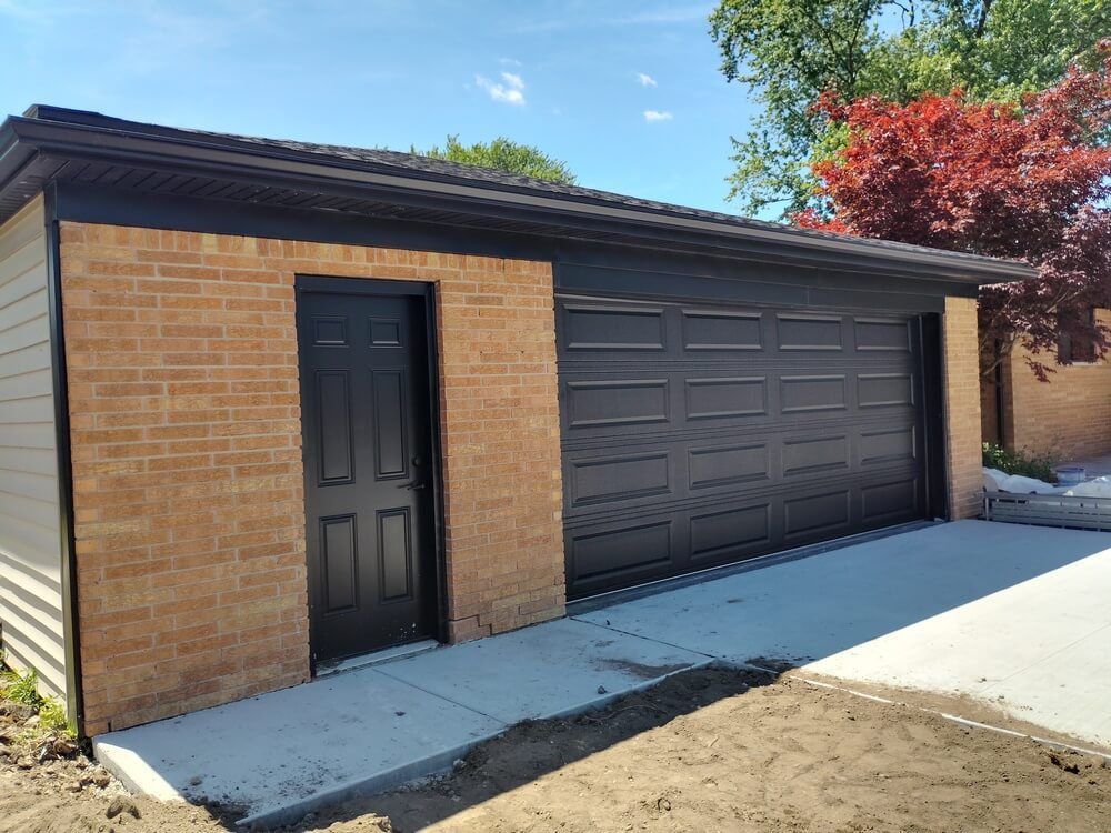 Single-story brick garage with a dark door and large dark roll-up door, beside a concrete driveway.